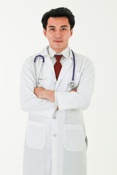 Portrait Of A Professional Medical Male Doctor Standing On White Background With Crossed Arms, Wearing White Gown Coat, And Stethoscope, Smiling, Looking At A Camera Proudly In His Occupation.