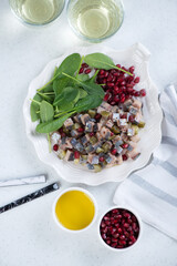 Herring tartar with pomegranate and fresh spinach on a shell-shaped plate, top view on a white stone background, vertical shot