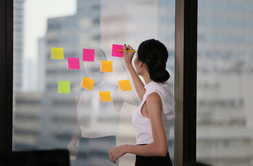 Business woman Write notes on the paper attached to the window glass.