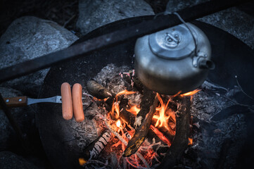 Metal kettle and grilled sausage on a campfire - 428951635