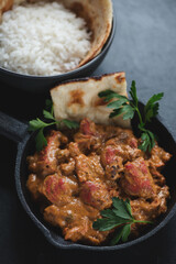 Closeup of a cast-iron skillet with indian butter chicken or Murgh Makhani, vertical shot on a black stone surface, selective focus
