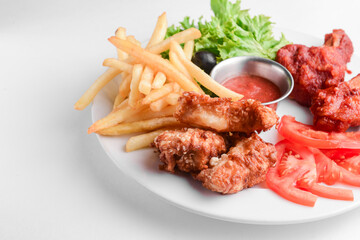 Roasted chicken wings and French fries isolated over white background. Served with fresh lettuce salad