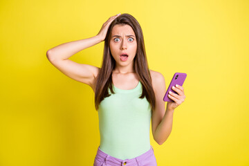 Photo of young attractive lovely amazed surprised girl see bad comment in phone isolated on yellow color background
