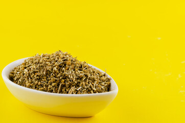 A mixture of dried medicinal herbs in a white ceramic bowl on a yellow background.