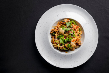 Sea food wok stir fry served in a white plate. Clams and shrimps wok isolated on black.