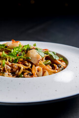 Sea food wok stir fry served in a white plate. Clams and shrimps wok isolated on black.