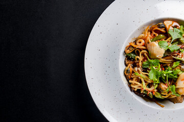 Sea food wok stir fry served in a white plate. Clams and shrimps wok isolated on black.