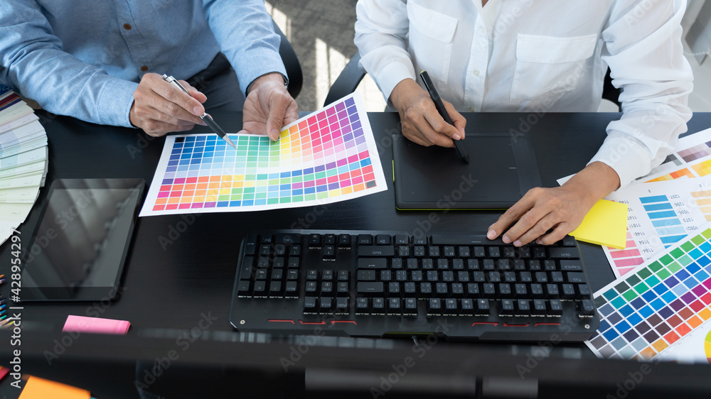 Poster graphic designer or creative working together coloring using graphics tablet and a stylus at desk wi