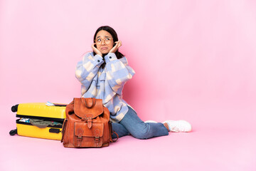 Traveler woman with a suitcase sitting on the floor frustrated and covering ears