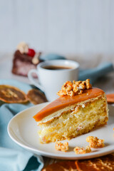 One piece of Caramel cake with pop corn on top served on a white plate. Dried oranges and a cup of Espresso coffee.
