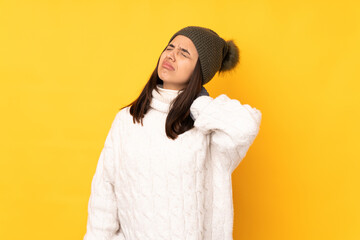 Young woman with winter hat over isolated yellow background with neckache