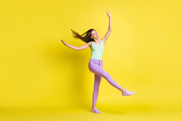 Fototapeta na wymiar Photo of funny cute lady dreamy dance raise hands wear green singlet pants sneakers isolated yellow color background