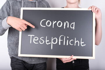 Schulkinder mit einer Tafel auf der Corona Testpflicht steht