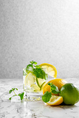 Citrus lemonade with ice in a glass decorated with lemon, lime and mint slices and on a marble table. Fresh summer drink. Detox. Healthy food rich in vitamins and antioxidants. Copy space