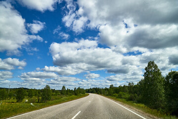 View from relief car windscreen on the blue sky with white clouds, grey asphalt road and landscape with forest and green teeses. Landscape through window