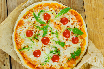 Round pizza with cheese and tomatoes on a wooden table, green basil leaves. View from above.