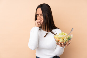 Young brunette girl holding a salad over isolated background is suffering with cough and feeling bad