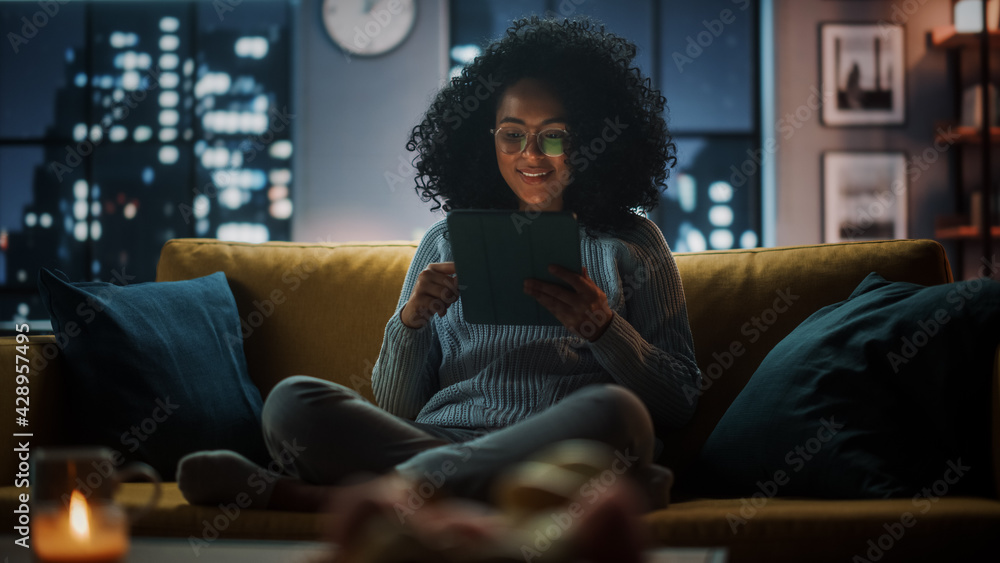 Poster beautiful authentic latina female sitting on couch sofa in a cozy dark living room in the evening an