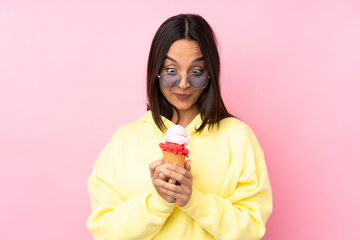 Young brunette girl holding a cornet ice cream over isolated pink background scheming something
