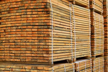Wooden boards are stacked in piles in workshop. Industrial background, business timber. Pine lumber for furniture production and construction. Folded wooden brown planks in a sawmill.