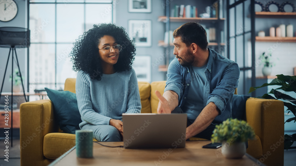 Poster diverse multiethnic couple are sitting on a couch sofa in stylish living room and choosing items to 