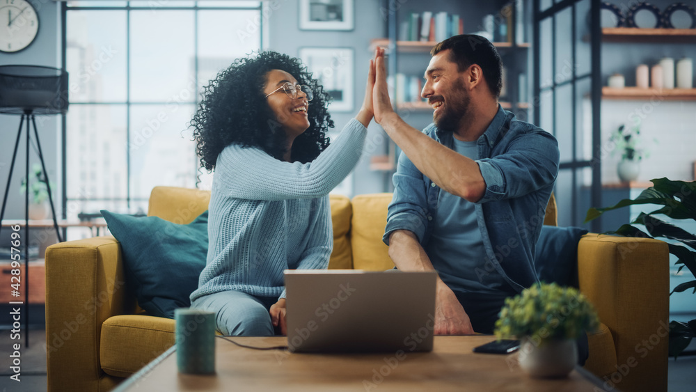 Poster diverse multiethnic couple are sitting on a couch sofa in stylish living room and choosing items to 