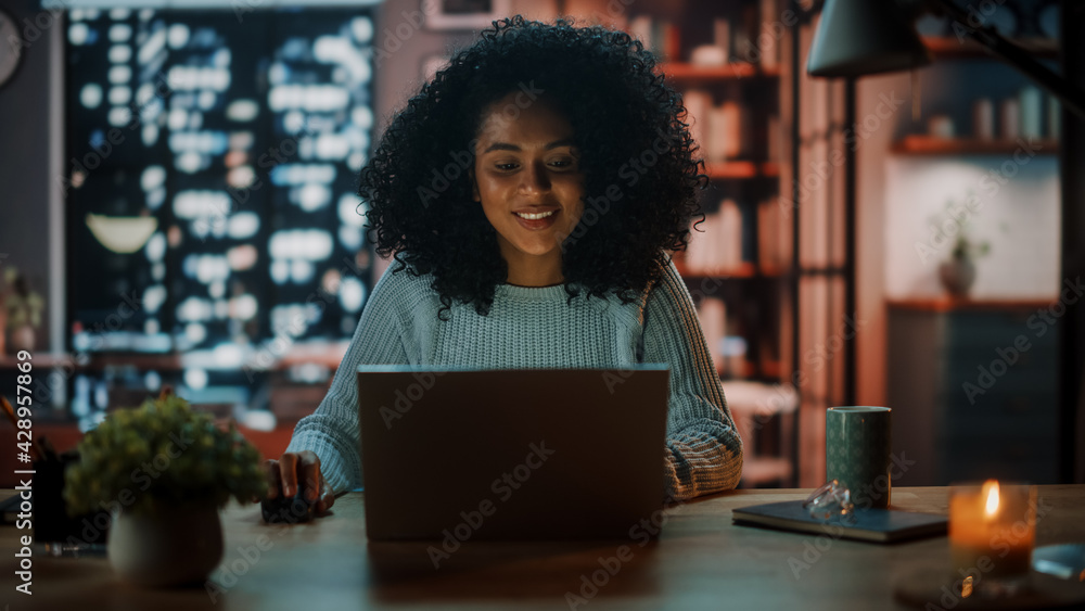 Poster beautiful authentic latina female sitting at a desk in a cozy dark living room in the evening and us