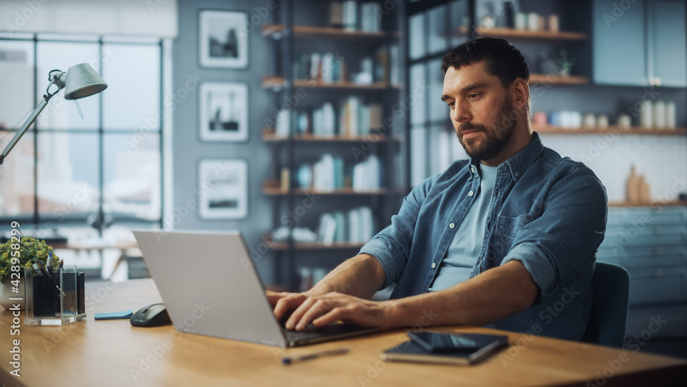 Poster handsome caucasian man working on laptop computer while sitting on a sofa couch in stylish cozy livi