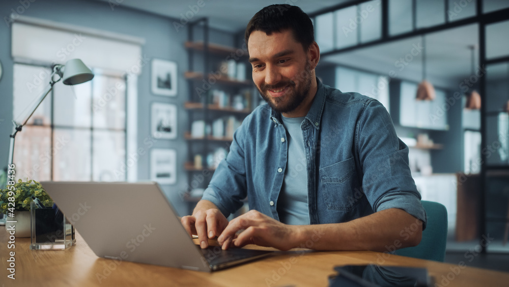 Poster handsome caucasian man working on laptop computer while sitting on a sofa couch in stylish cozy livi