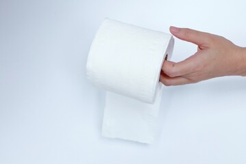 Hand holding a roll of toilet paper on a white wall.