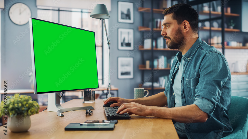 Poster handsome caucasian specialist working on desktop computer with green screen mock up display at home 