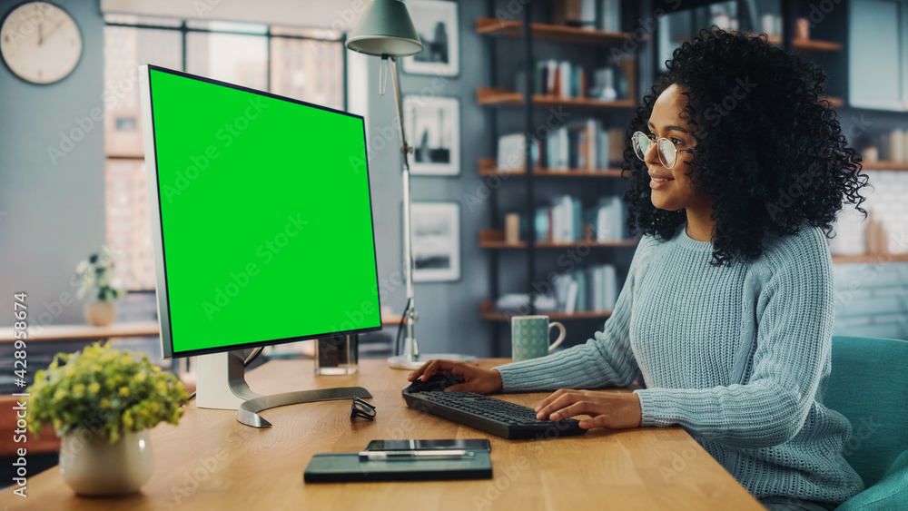 Poster latina female specialist working on desktop computer with green screen mock up display at home livin