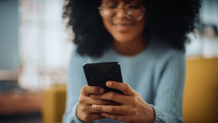 Portrait of a Beautiful Authentic Latina Female with Afro Hair in Stylish Cozy Living Room Using Smartphone at Home. She's Browsing the Internet and Checking Videos on Social Networks and Having Fun.