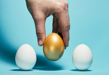 The hand chooses the golden egg among the white eggs.Concept of exclusivity, best choice, hiring.