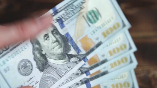 Women's hands count money: they shift dollars on a wooden table, flip through bills. One hundred dollars. A stack of $ 100 bills in close-up. Finance, economy, financial planning, economics, savings.