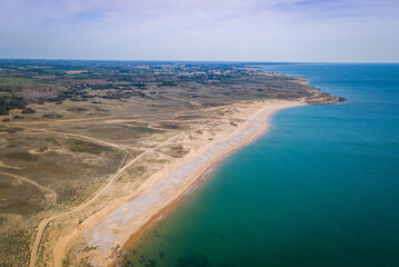 Fototapeta na wymiar Aerial photography of sunny beach from above with clear water, sandy dunes behind and a small village in the background