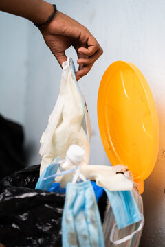 Close up of healthcare worker or doctor hands throwing single use disposable medical face mask and gloves into filled trash can or garbage bin at hospital during coronavirus covid-19 pandemic.