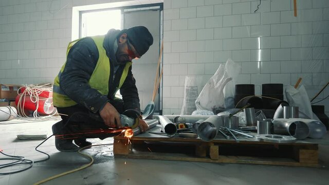 Male locksmith working in production. A man cuts a metal pipe with his hand without protection. Sparks flying off cutting a metal pipe.