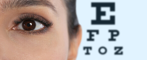 Closeup view of woman and blurred eye chart on background, banner design. Visiting ophthalmologist