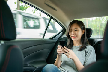 Fototapeta na wymiar Asian woman sitting in a car is delighted after seeing a message on her cell phone.