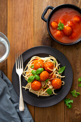 Meatballs with tomato sauce and spaghetti, pasta in black mate plate on wooden background, delicious mediteranean food