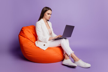 Close up profile portrait of lady sit beanbag hold netbook work project on violet wall