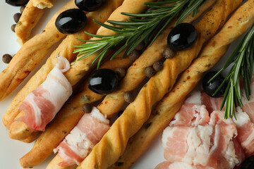 Tasty grissini with bacon and snacks, close up
