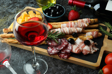 Board with grissini and snacks, and wine on black smokey background