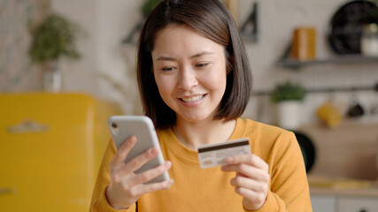 Multi ethnic female client holding banking credit card and smart phone involved in verification process in mobile application. Asian young woman doing payments online or shopping in internet store
