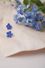 Beautiful Forget-me-not flowers and parchment on white wooden table, closeup