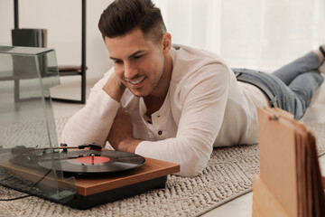 Fototapeta na wymiar Happy man listening to music with turntable while lying on floor at home