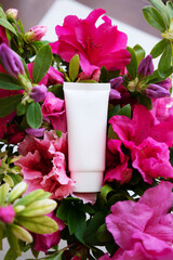 white cosmetic tube for face cream, body wash, face mask or body lotion on a background strewn with flowers. The concept of a flavored cosmetic product