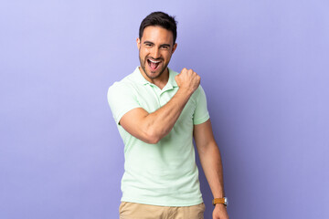 Young handsome man isolated on purple background celebrating a victory