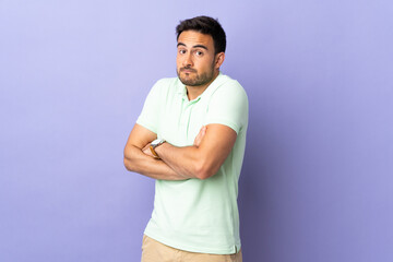 Young handsome man isolated on purple background making doubts gesture while lifting the shoulders